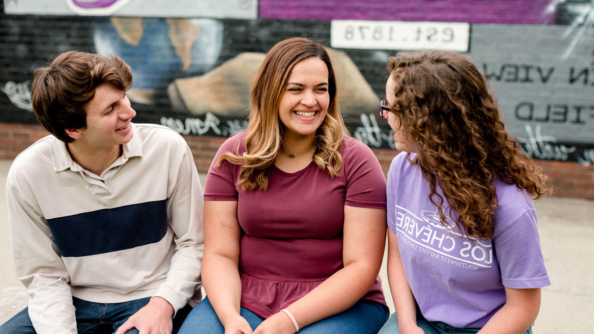 三个学生微笑着坐在砖墙壁画前